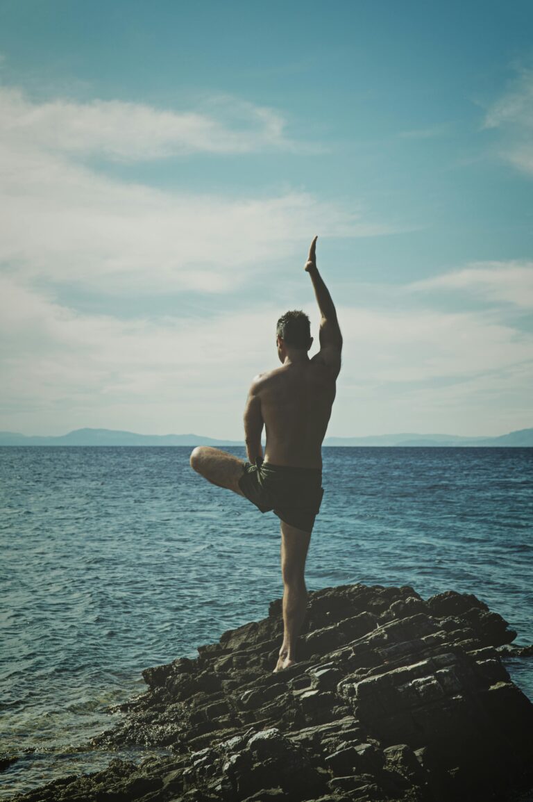 Back view of a man practicing yoga on a rocky seashore. Embracing peace, meditation, and nature.