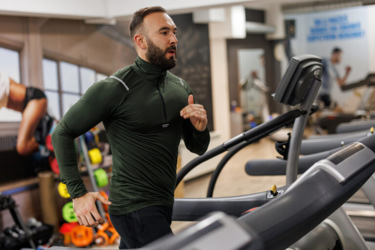 Young sports man running on a treadmill at gym